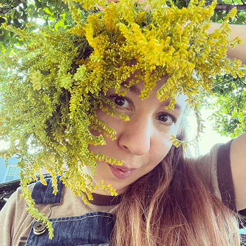 sunny photo of jess erin holding a spray of goldenrod around their face